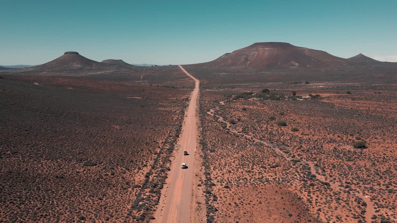 Two vehicles drive on a vast, empty dirt road in the middle of nowhere in South Africa