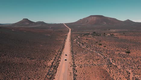 two vehicles drive on a vast, empty dirt road in the middle of nowhere in south africa