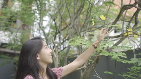 female smiling and touching flowers on a green tree during a warm summer