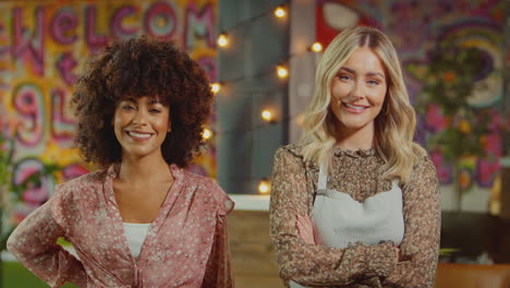 Portrait-Of-Smiling-Female-Server-And-Owner-Wearing-Apron-Standing-In-Cool-Bar-Or-Club