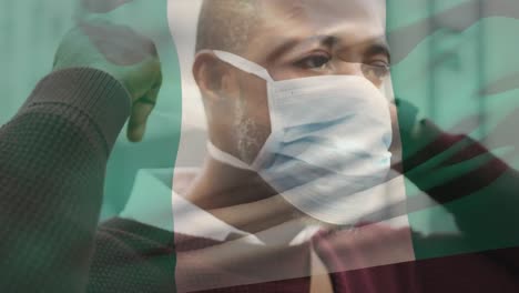 Animation-of-flag-of-nigeria-waving-over-man-wearing-face-mask-during-covid-19-pandemic