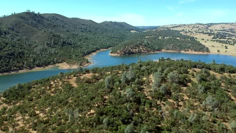 Slowly-flying-over-hills,-trees,-sand-and-a-curved-lake