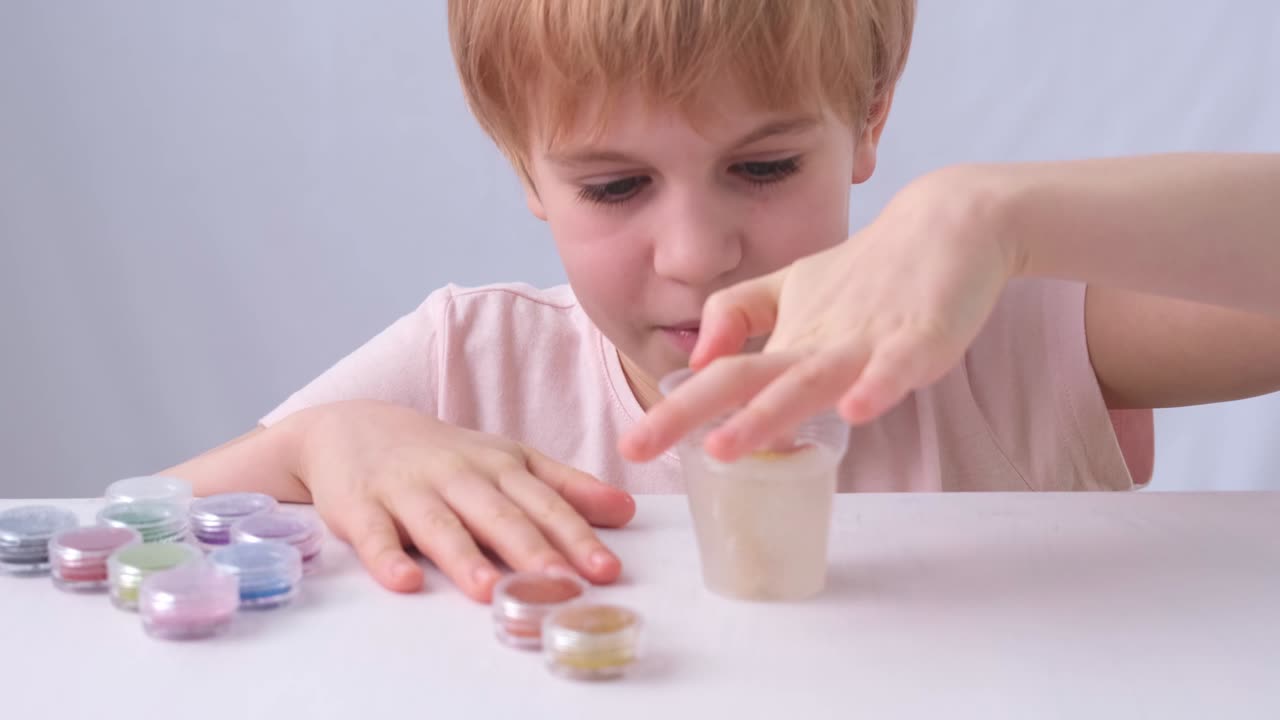 The child's hands are close-up. A child of primary school age takes the slime out of the jar. A slic of different colors. The child lays out the toy on the table in front of him. Touch, emotion