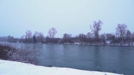 snow falling in storm by river, slow motion, still shot