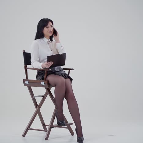 portrait of a beautiful businesswoman with a phone. young woman sitting in the chair with a black folder and talking the mobile phone indoors.