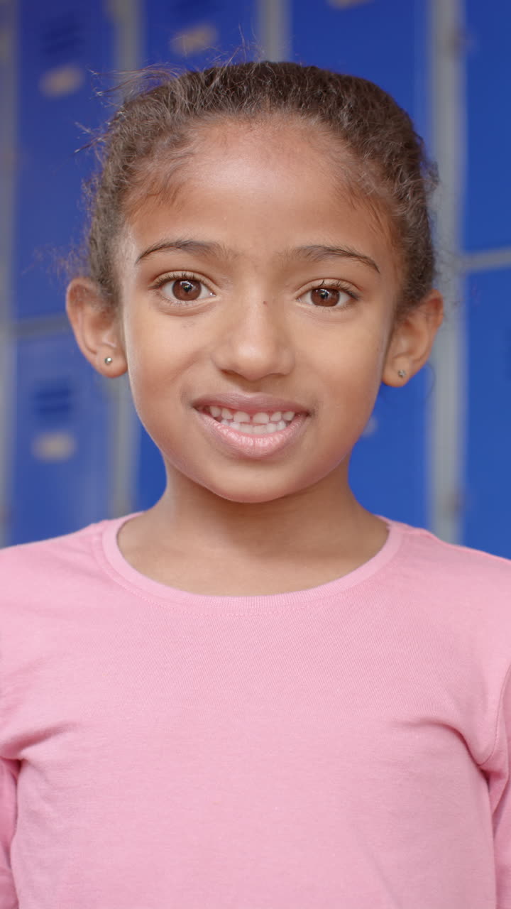 Vertical video: In school, young biracial female student standing, blue background