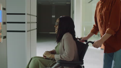 Mujer-Empujando-A-Un-Colega-En-Silla-De-Ruedas-En-El-Centro-De-Oficinas