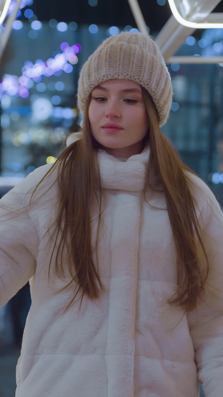 Stylish woman in cozy winter outfit passing through illuminated star decoration in vibrant city, background features colorful lights, moving cars, and pedestrians in a festive urban setting at night