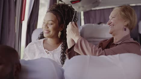 two women smiling and interacting with a smartphone on a bus trip
