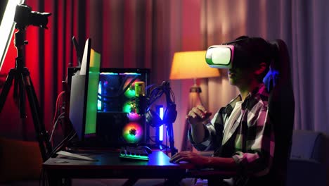 side view of asian boy streamer playing game, touching, and swiping experience virtual reality in futuristic goggles. green screen personal computer on desk illuminated by rgb led strip light