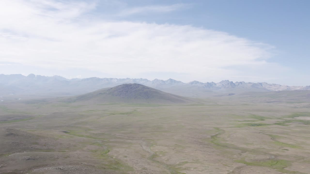 Wide aerial view of Deosai’s flat plains with a lone hill and distant mountain range. Gilgit-Baltistan, Pakistan