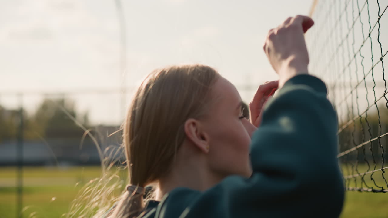 강렬한 훈련 중에 점프하는 여자들의 클로즈업, 전면에 볼리볼 네트, 모션 블러는 액션을 강조하고, 빛이 머리카락에서 반사되며, 배경에는 스포츠 시설이 있습니다.