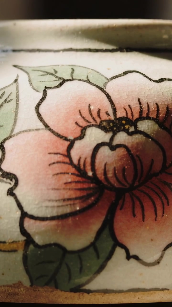 縦型動画：カメラがテーブル上の容器をスライドしながらスキャンし、描かれたピンクの花と金色の縁取りを見せる