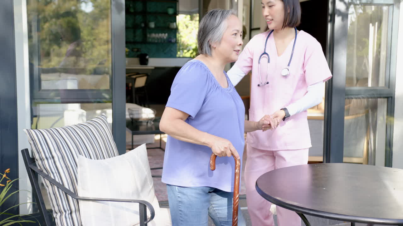 Helping senior asian woman with cane, nurse in pink scrubs smiling outdoors