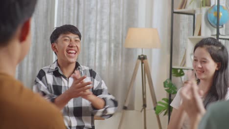 close up of asian teen group sitting in chairs forming a circle discussing at home. celebrating, applause or audience clapping hands after a boy in plaid shirt giving speech