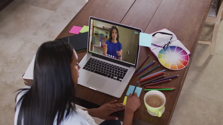 African american woman writing on memo notes while having a video call on laptop at home