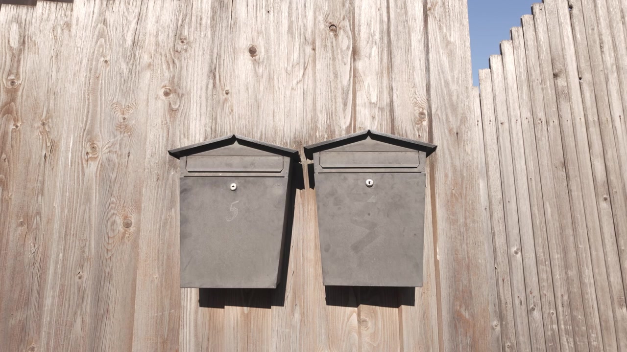 Two metal mailboxes mounted on wooden fence outside residential property