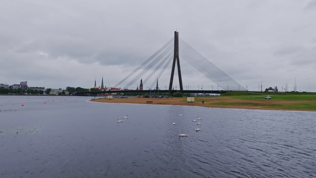 Overcast Riga cityscape reflects calm mood on Daugava waters beneath bridge