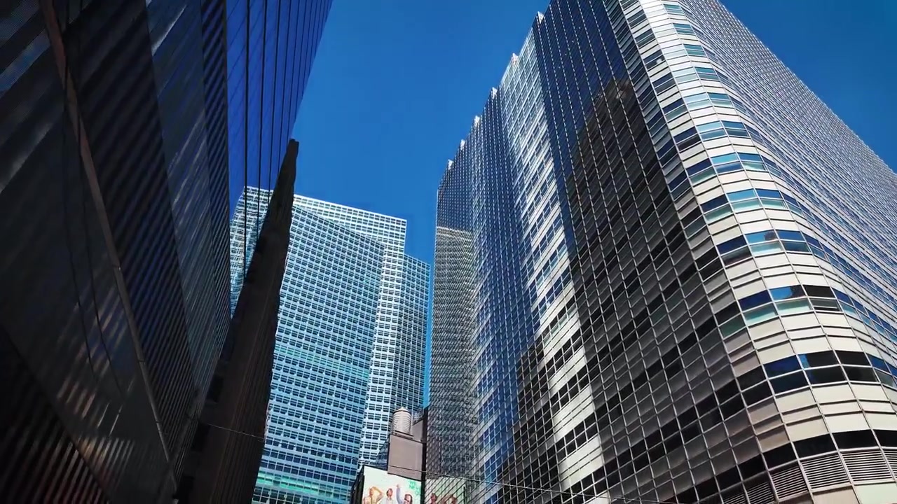 Langsom opadgående kamerapanorering, der afslører moderne glasskyskrabere og reflekterende kontortårne i Manhattan West nær Hudson Yards, New York City, under en klar blå himmel.