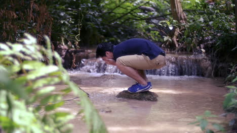 man washing face in a forest stream
