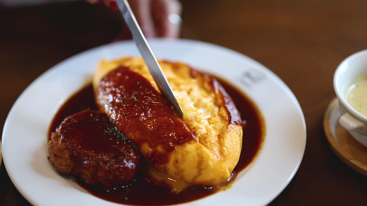 Hand slices omurice and hamburg steak in demi-glace sauce, natural lighting, close-up view
