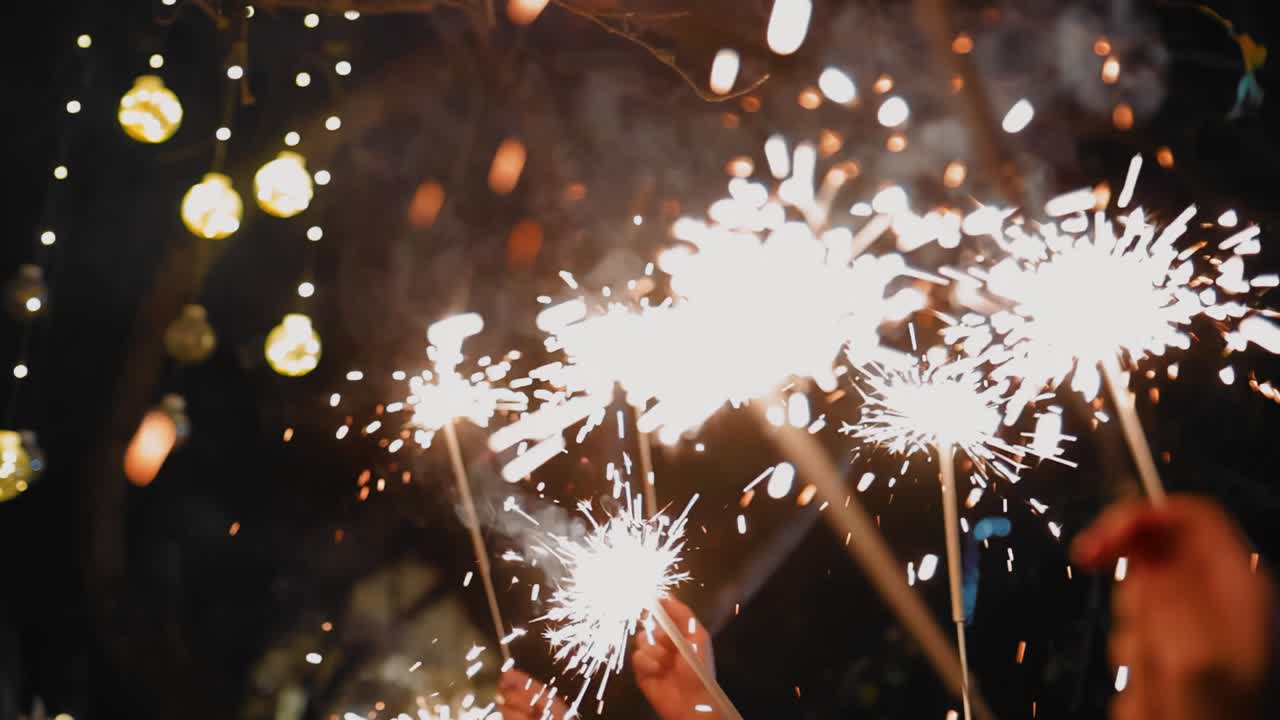 A crowd of people raised their hands with burning sparklers above them. Shooting a holiday and sparks from sparklers