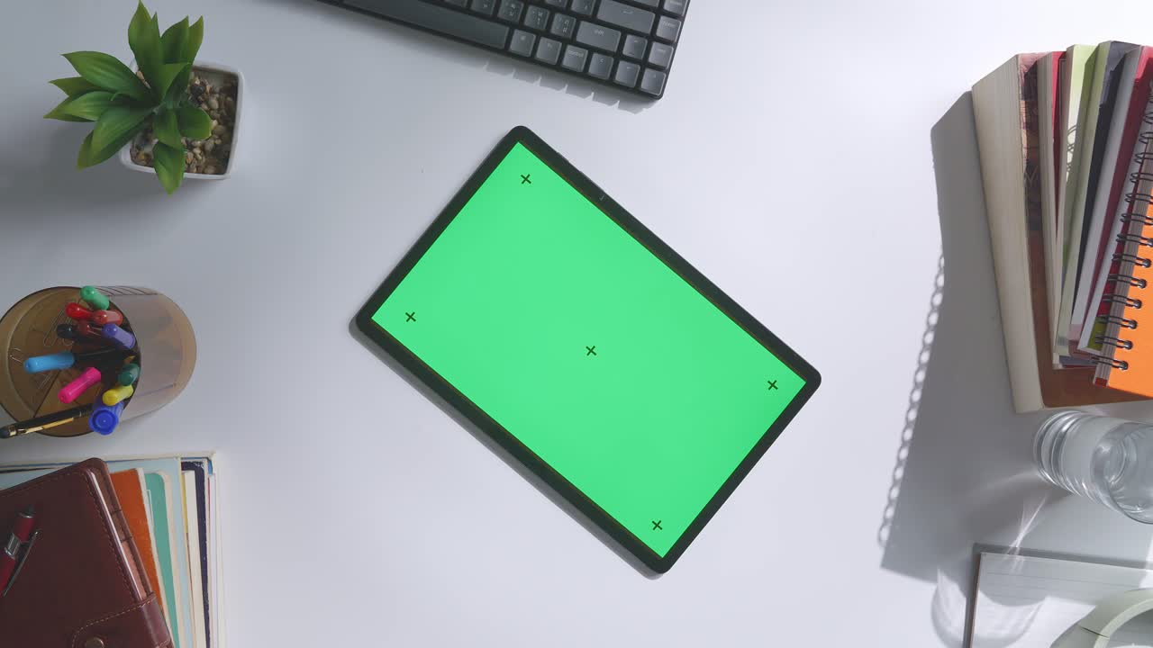 vista de arriba hacia abajo de una computadora portátil con pantalla verde simulada pantalla chromakey en un escritorio de oficina de madera al lado de la libreta con bolígrafos, gafas y un vaso de agua.