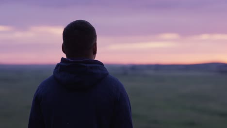 man contemplating sunrise over field