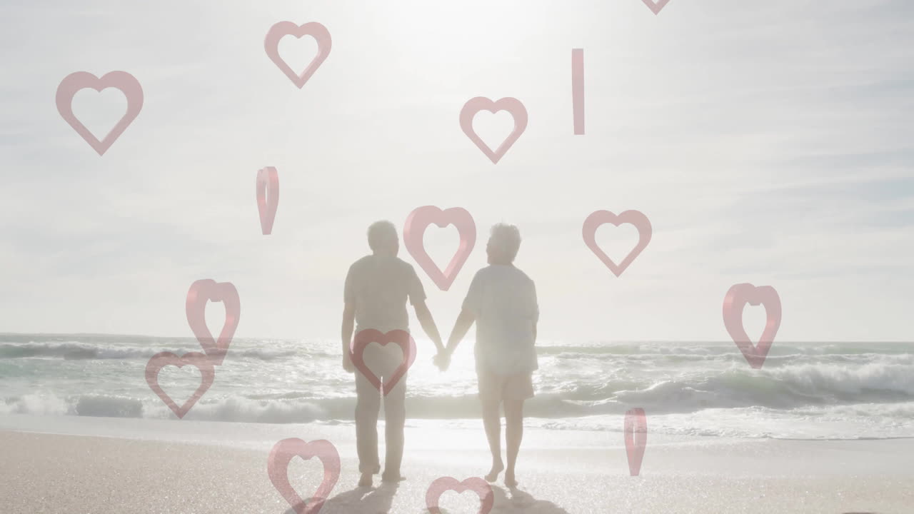 Elderly couple holding hands on beach with heart shapes overlay animation