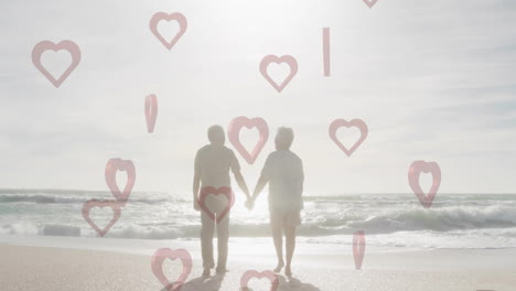 elderly couple holding hands on beach with heart shapes overlay animation