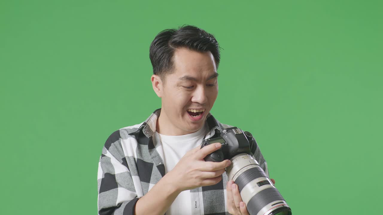 스튜디오에서 녹색 화면 배경에 서있는 동안 카메라에서 사진을 보는 후 와우라고 말하는 아시아 사진작가의 클로즈업