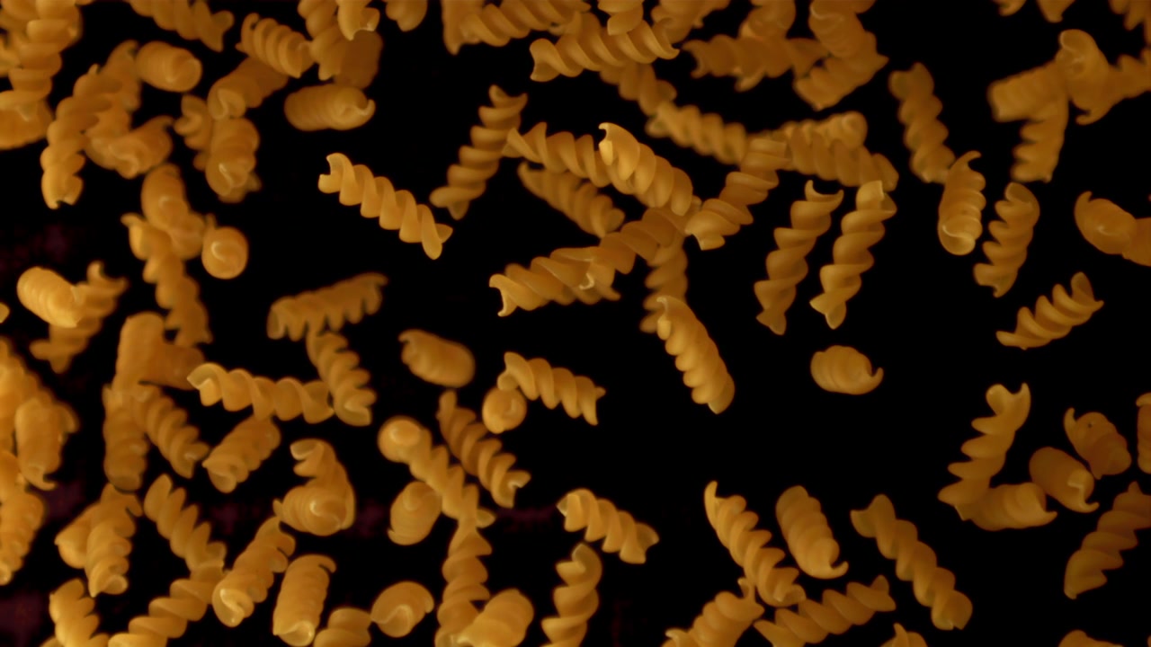 Fusilli che cadono al rallentatore su sfondo nero.