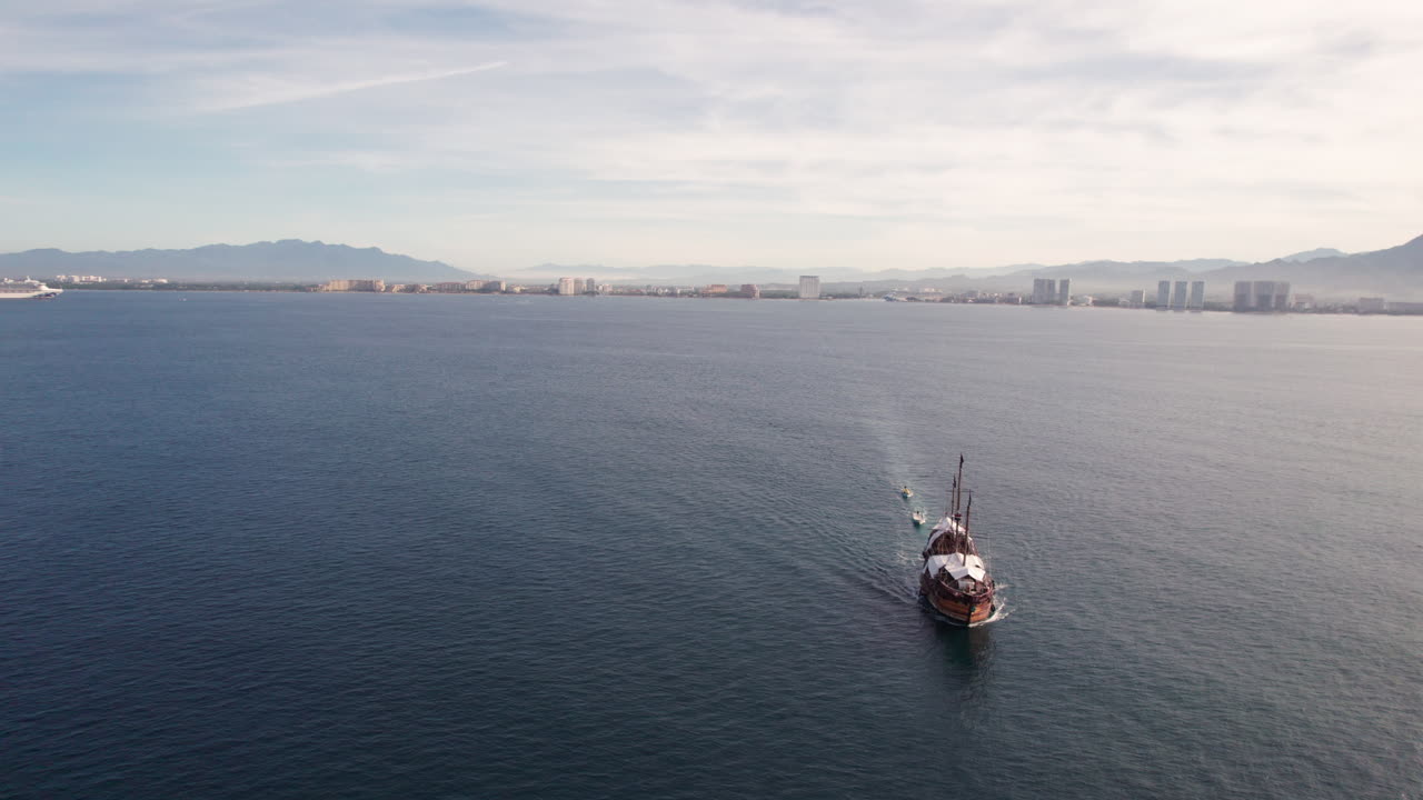 A pirate-style wooden ship is shown sailing along the coasts of Puerto Vallarta, Jalisco and Bah&iacute;a de Banderas, Nayarit, with the drone orbiting the impressive vessel, showing the distant coastline
