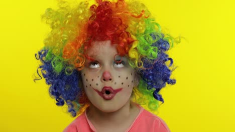 little child girl clown in wig making silly faces. fool around, singing, showing tongue. halloween