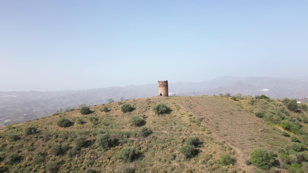 Drone reveal shot of the rural outskirts of Malaga. The remains of a medieval tower stands on top of the hill.