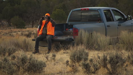 hunter filming how two men carry a dead deer buck towards the pick up for transportation