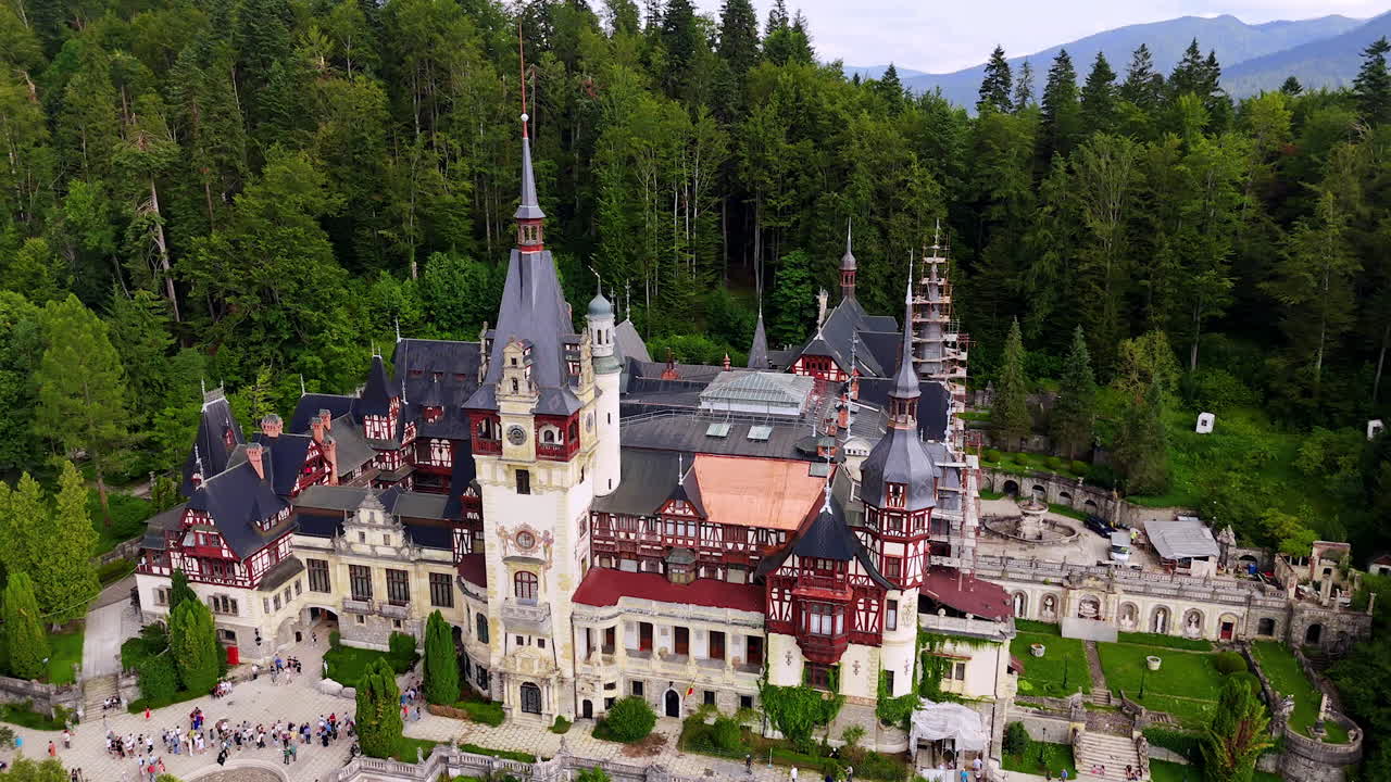 Multiple tourists wait in line to enter the Pele? Castle in the Carpathian Mountains, Romania. Aerial perspective on the landmark from drone