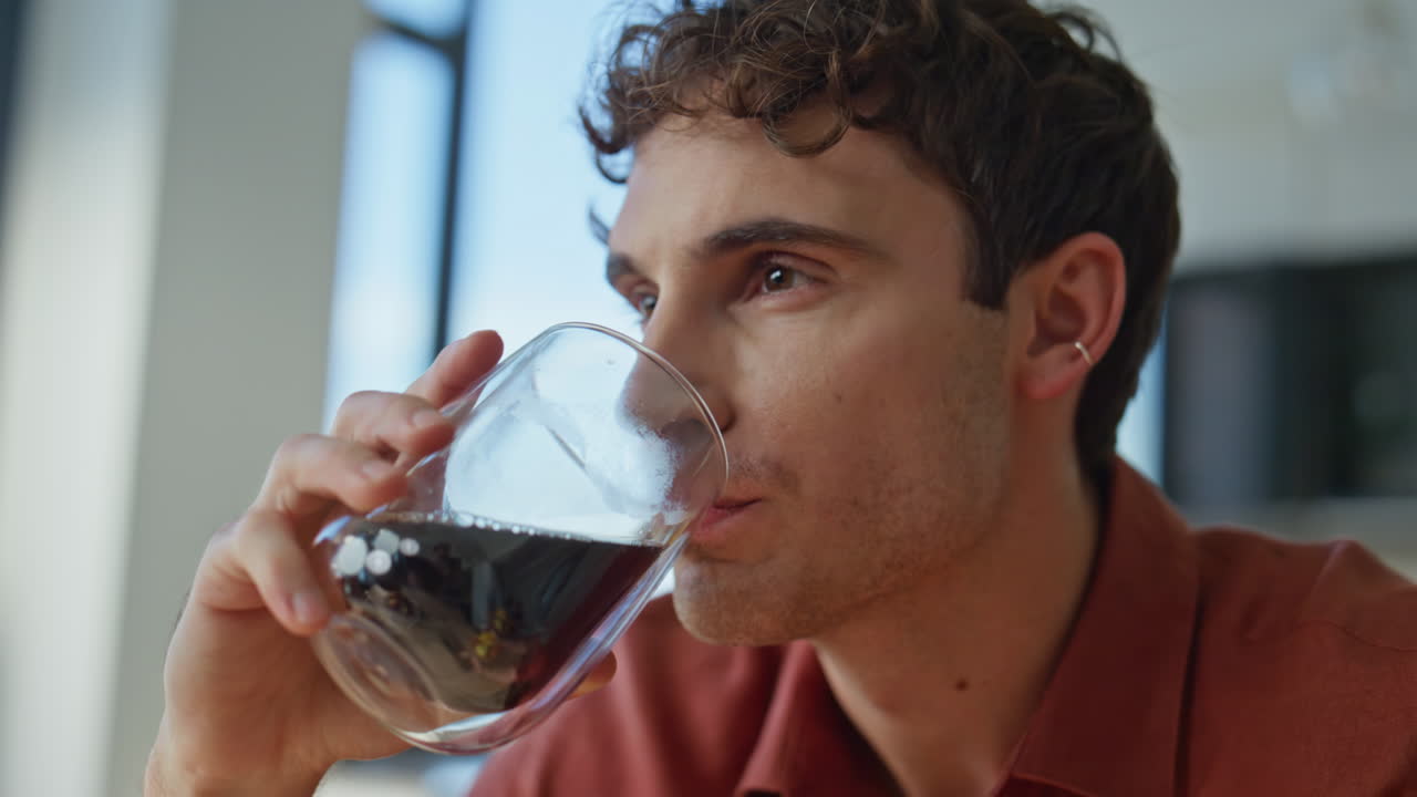 Portrait cheerful man drinking coffee in apartment kitchen. Relaxed hipster