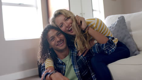 Portrait-of-happy-diverse-couple-embracing-and-sitting-on-couch-at-home,-slow-motion