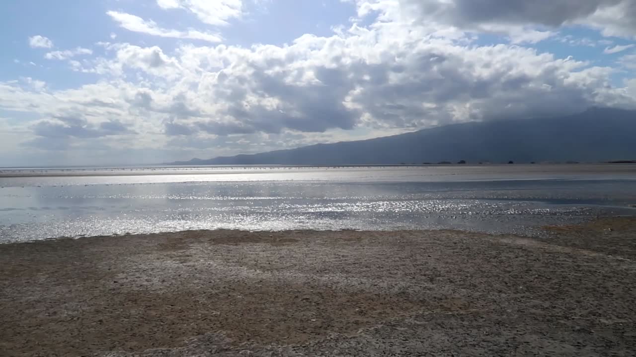 panorámica a la derecha en una orilla del lago natron con montañas de tanzania cubiertas de nubes