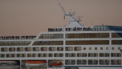 passengers standing along top deck of cruise ship during golden hour