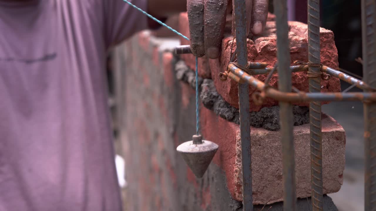 close up of indian labor in construction site making manual Plumb Bob measurement calculating distance from the brick wall