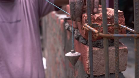 primer plano de la mano de obra india en el sitio de construcción haciendo medición manual de plomo bob calculando la distancia desde la pared de ladrillo