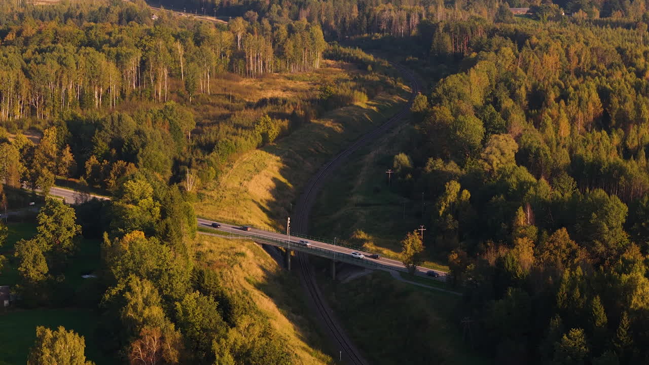 Car driving on bridge over railway line in woodland area, aerial view