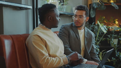 two male colleagues discussing project on laptop in comfortable office