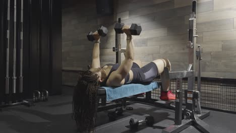 woman lying on a bench performing dumbbell chest presses in a gym environment