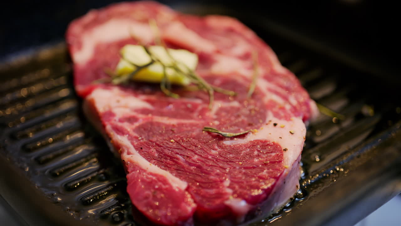 Butter melting on a seasoned steak cooking on a hot grill pan with rosemary herbs