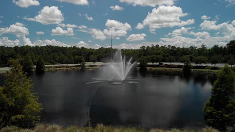 slow push in passing by trees on side revealing water fountain in pond with trees around water