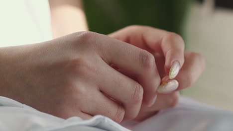 woman with shiny manicure taps fingers sitting in light room