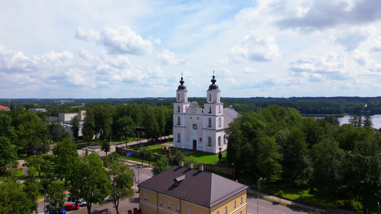 Drone view of the central square in Zarasai featuring colorful buildings and a white church framed by trees. Shot at Zarasai, Lithuania (Zarasai, Lietuva)